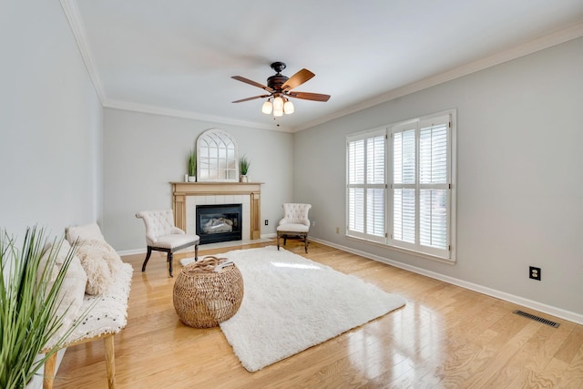 sitting room featuring light wood finished floors, crown molding, baseboards, and a tiled fireplace