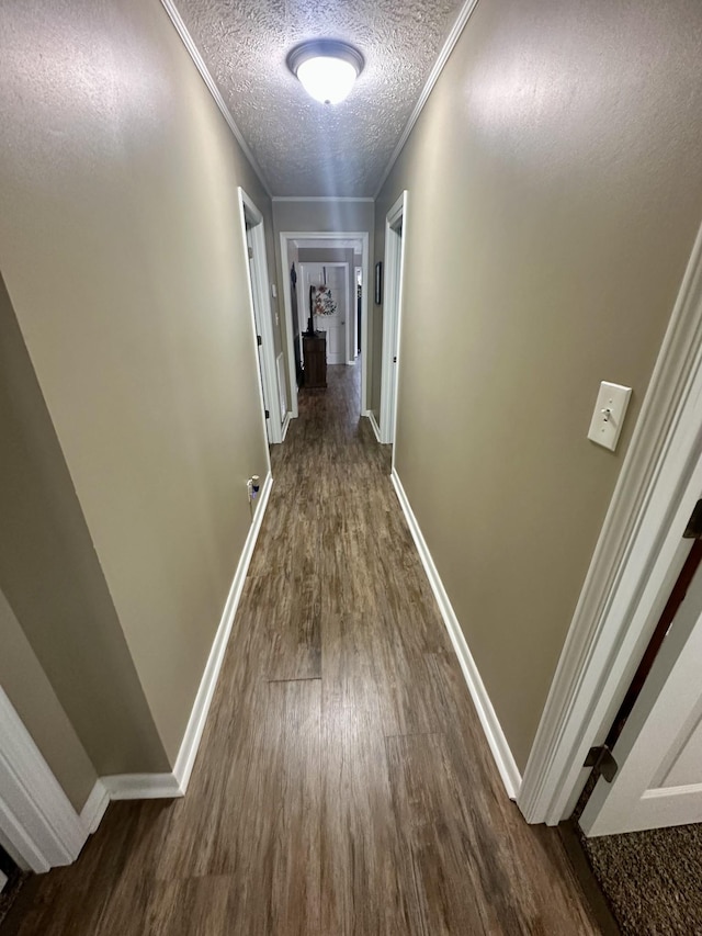 hallway with a textured ceiling, baseboards, dark wood-style flooring, and crown molding