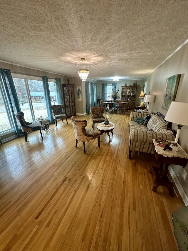 living area featuring a textured ceiling, ornamental molding, light wood-type flooring, and an inviting chandelier