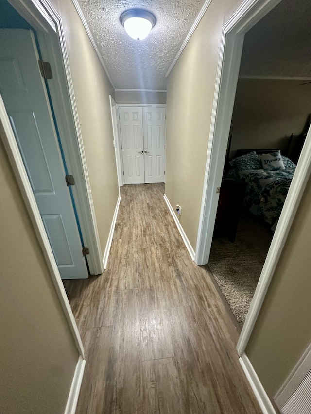 corridor with crown molding, a textured ceiling, baseboards, and wood finished floors