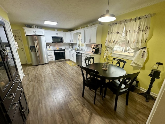 kitchen featuring tasteful backsplash, appliances with stainless steel finishes, white cabinets, a sink, and wood finished floors