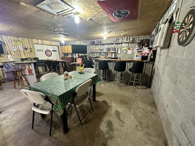 dining area with a dry bar, unfinished concrete flooring, and concrete block wall