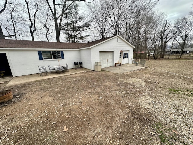 rear view of house with a garage, driveway, concrete block siding, and a patio