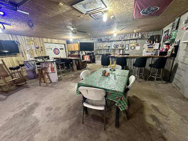 dining area with concrete block wall, a dry bar, and unfinished concrete floors