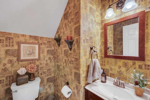 half bathroom featuring lofted ceiling, vanity, toilet, and wallpapered walls