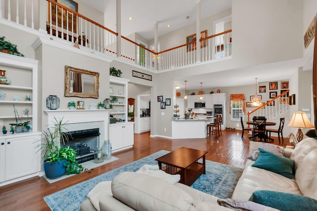 living area with baseboards, built in features, a fireplace with flush hearth, dark wood-style flooring, and stairs