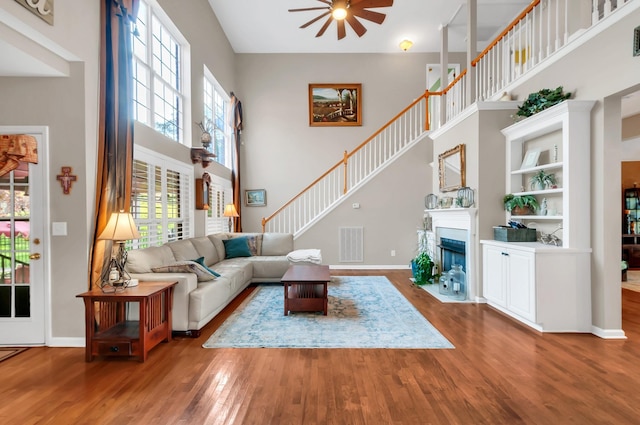 living area with visible vents, a ceiling fan, a fireplace with flush hearth, wood finished floors, and a high ceiling