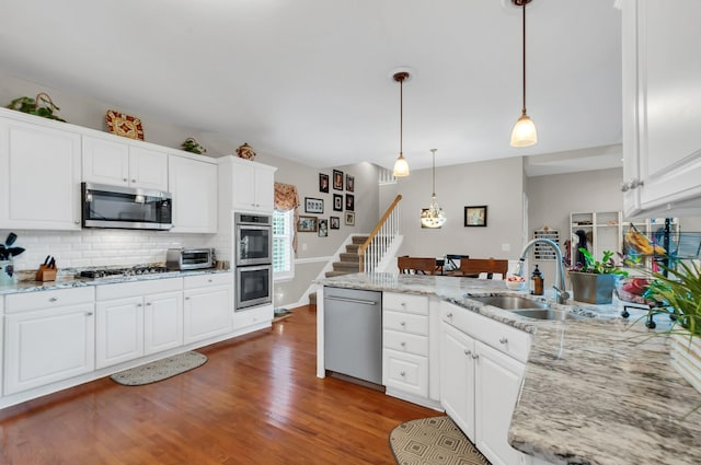 kitchen with stainless steel appliances, a peninsula, wood finished floors, a sink, and decorative backsplash