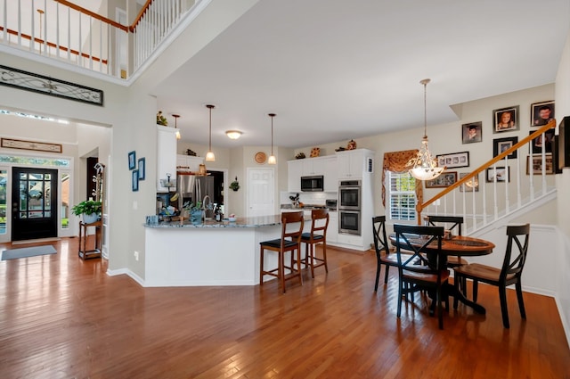 kitchen with light stone counters, stainless steel appliances, white cabinetry, wood finished floors, and a peninsula