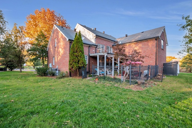 rear view of house featuring a yard, brick siding, and fence