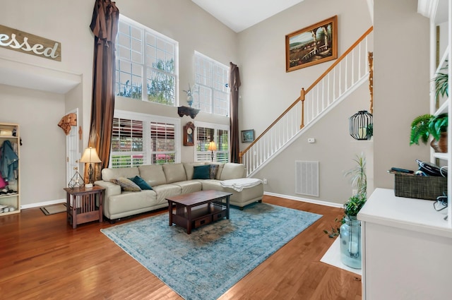 living room with a high ceiling, wood finished floors, visible vents, and baseboards