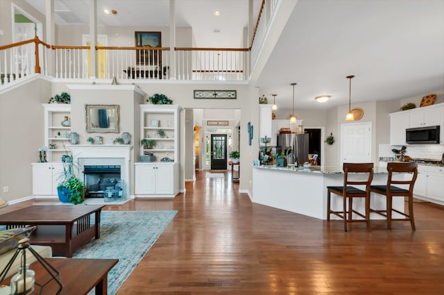 living room featuring a towering ceiling, a fireplace with flush hearth, baseboards, and dark wood-type flooring