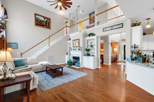 living room with light wood-style floors, visible vents, a fireplace with flush hearth, and a ceiling fan