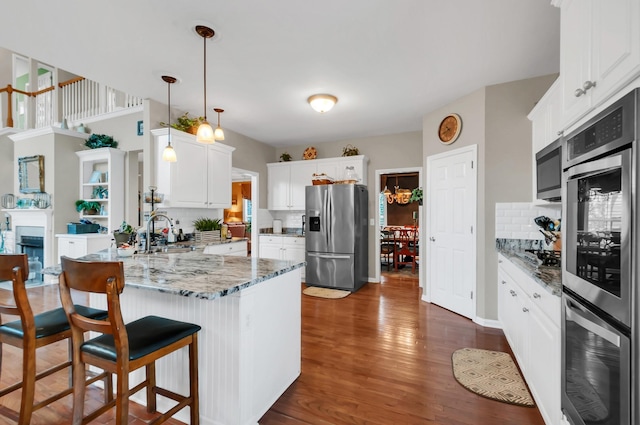 kitchen featuring dark wood finished floors, a fireplace, appliances with stainless steel finishes, a sink, and a peninsula