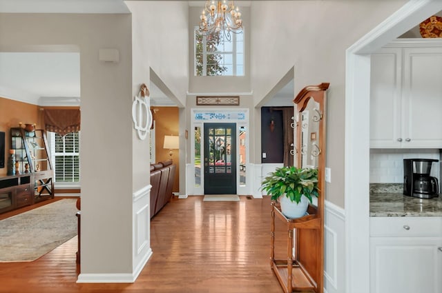 foyer featuring a wainscoted wall, a decorative wall, light wood-style flooring, a towering ceiling, and an inviting chandelier