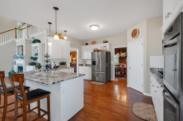 kitchen with a peninsula, appliances with stainless steel finishes, decorative backsplash, and dark wood-style flooring