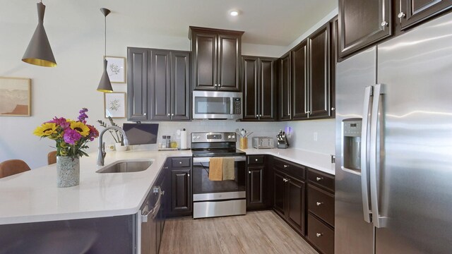 kitchen with stainless steel appliances, a peninsula, a sink, light countertops, and light wood finished floors