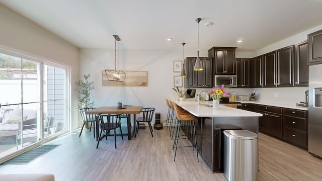 kitchen featuring appliances with stainless steel finishes, a breakfast bar, light countertops, and dark brown cabinetry