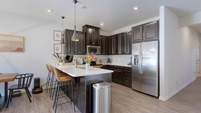 kitchen featuring dark brown cabinetry, a peninsula, stainless steel appliances, light countertops, and a kitchen bar