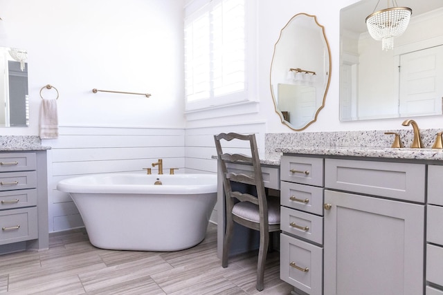 full bath featuring a wainscoted wall, a freestanding tub, vanity, and a notable chandelier