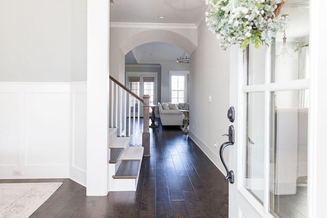 foyer featuring arched walkways, crown molding, dark wood finished floors, stairway, and wainscoting