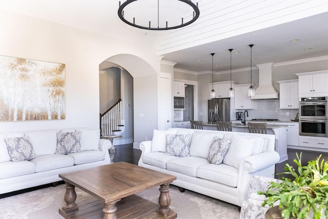 living room featuring arched walkways, crown molding, baseboards, and stairs