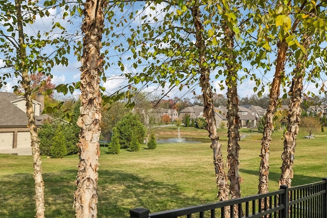 view of yard featuring a water view, a garage, fence, and a residential view