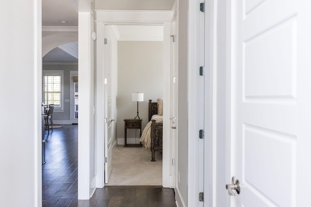 hallway featuring baseboards, ornamental molding, arched walkways, and dark wood-style flooring