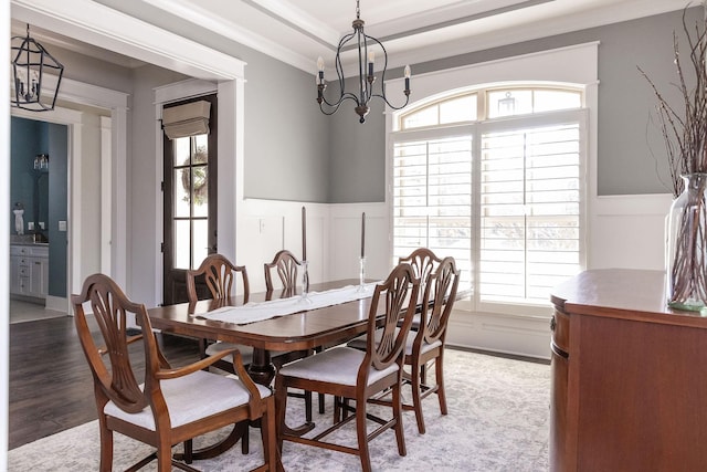 dining space featuring a decorative wall, ornamental molding, wainscoting, wood finished floors, and a chandelier