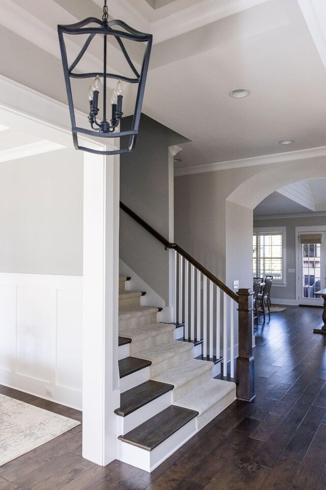 stairway with ornamental molding, arched walkways, wainscoting, and wood finished floors