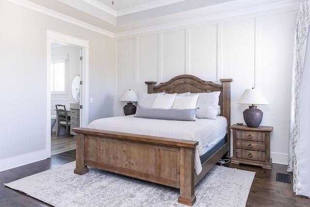 bedroom with visible vents, connected bathroom, wood finished floors, crown molding, and a decorative wall