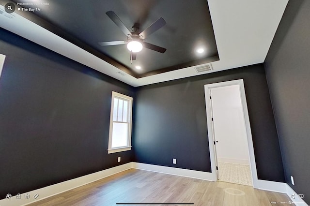 unfurnished room featuring a tray ceiling, baseboards, and wood finished floors