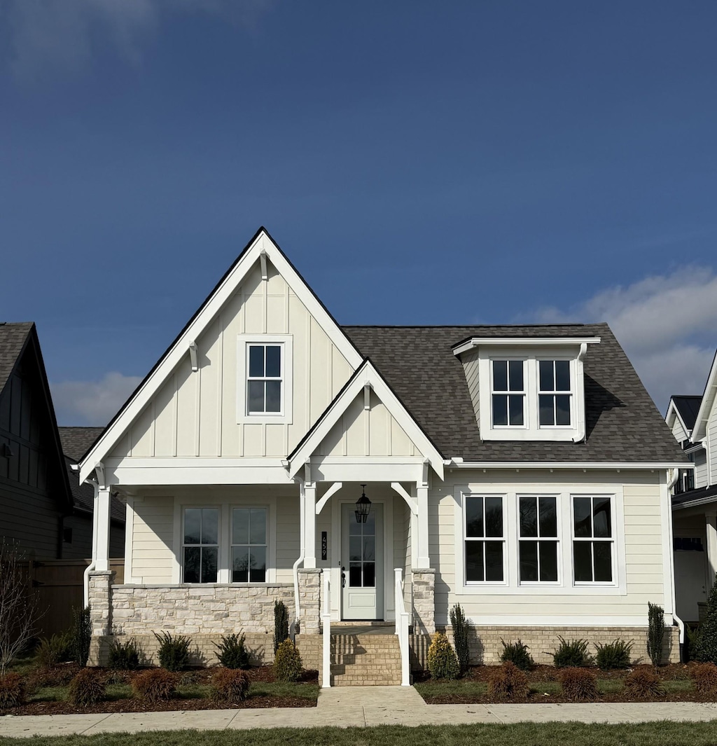 view of front of home featuring covered porch, stone siding, a shingled roof, and board and batten siding