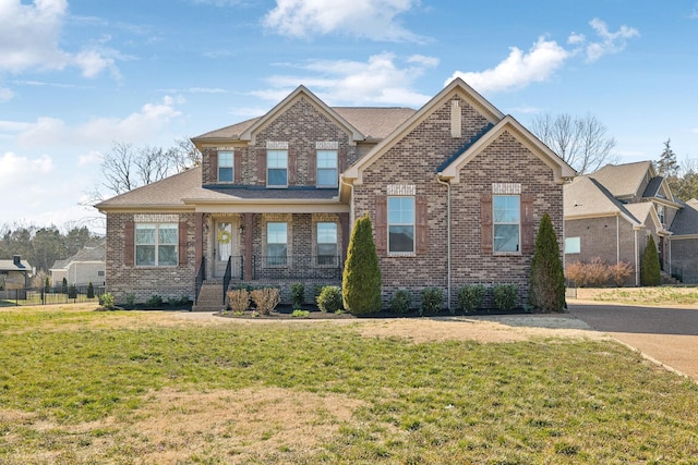 craftsman inspired home with brick siding, a porch, a front lawn, and fence