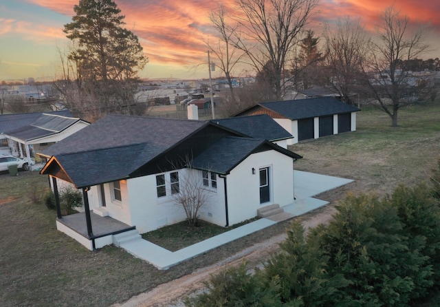 exterior space with an outbuilding, a garage, a shingled roof, stucco siding, and a front yard