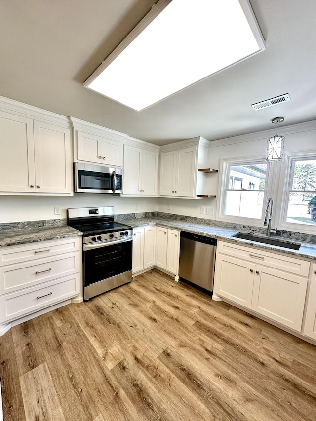 kitchen with stainless steel appliances, a sink, visible vents, white cabinets, and light wood finished floors