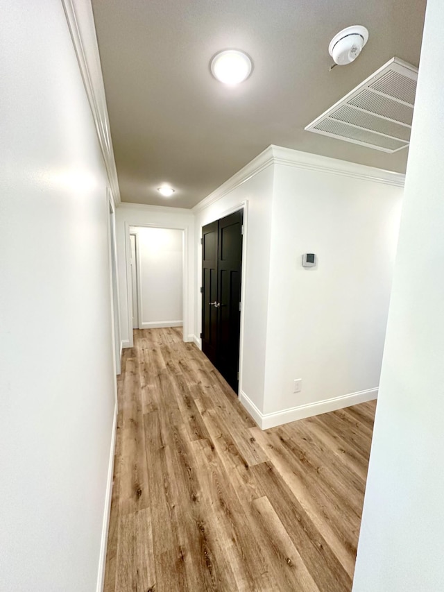 hall with baseboards, light wood-style floors, visible vents, and crown molding