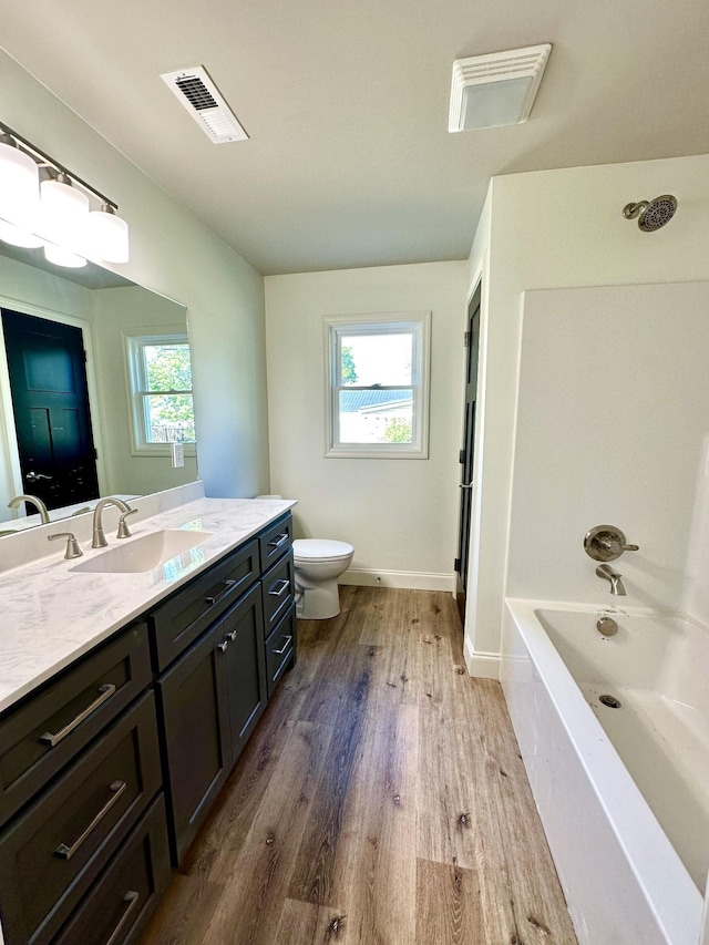 full bathroom featuring visible vents, toilet, a bathing tub, wood finished floors, and vanity