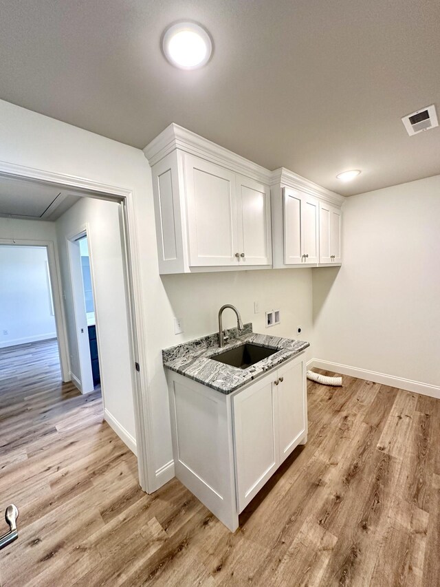 kitchen with a sink, visible vents, white cabinets, light wood-type flooring, and light stone countertops