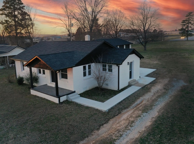 view of front of home featuring dirt driveway, a shingled roof, and a front lawn