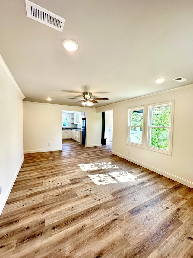 empty room with ornamental molding, visible vents, baseboards, and wood finished floors