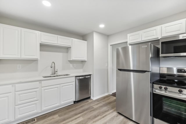 kitchen with light wood finished floors, appliances with stainless steel finishes, a sink, and white cabinets