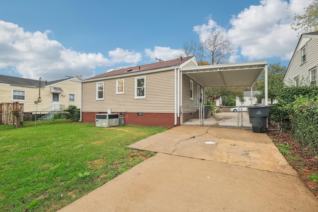 rear view of property featuring an attached carport, central air condition unit, fence, a lawn, and a gate