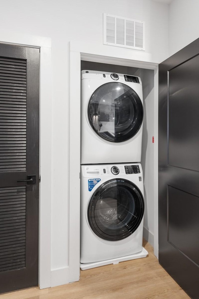 laundry room with visible vents, laundry area, stacked washer / drying machine, and wood finished floors