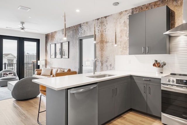 kitchen with gray cabinetry, open floor plan, appliances with stainless steel finishes, wall chimney exhaust hood, and a sink