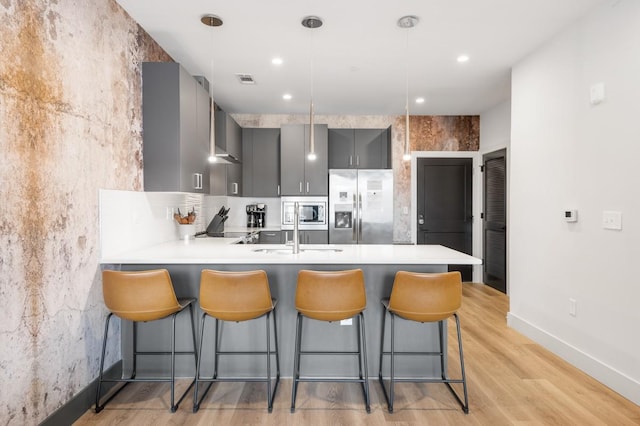 kitchen with a peninsula, gray cabinets, stainless steel appliances, light countertops, and a kitchen bar