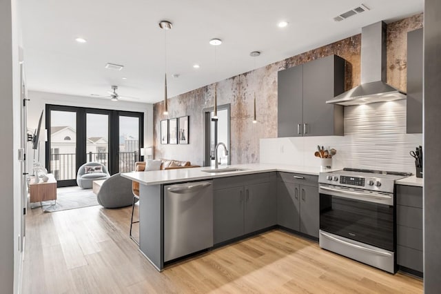 kitchen with visible vents, gray cabinets, stainless steel appliances, wall chimney exhaust hood, and a sink