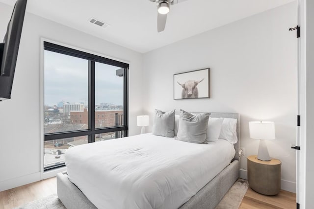 bedroom featuring baseboards, visible vents, light wood-style flooring, ceiling fan, and a view of city