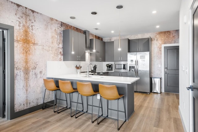 kitchen with gray cabinets, a sink, stainless steel appliances, a peninsula, and wall chimney range hood