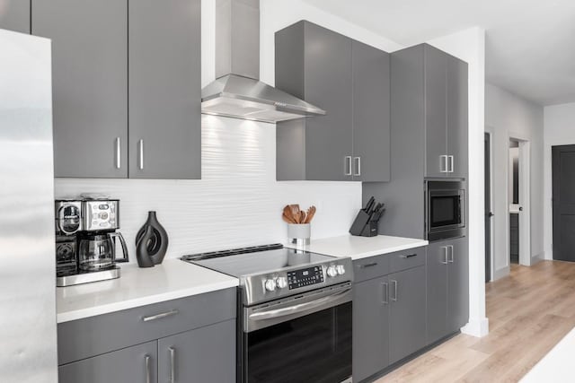 kitchen with light wood-style flooring, wall chimney exhaust hood, stainless steel appliances, light countertops, and gray cabinetry